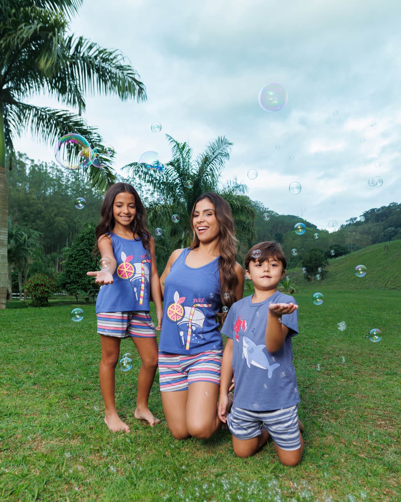 Mãe e dois filhos com pijama curto estampado azul no gramado, coleção Delícias de Verão